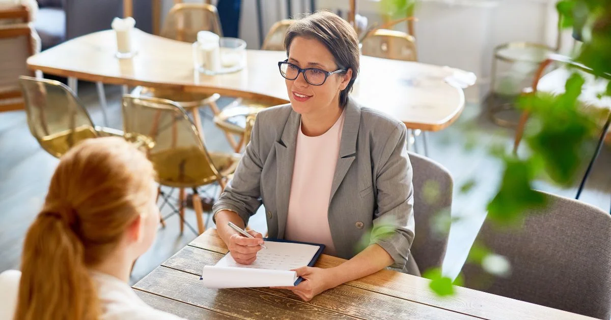 Recruiter interviewing candidate at table with notepad.